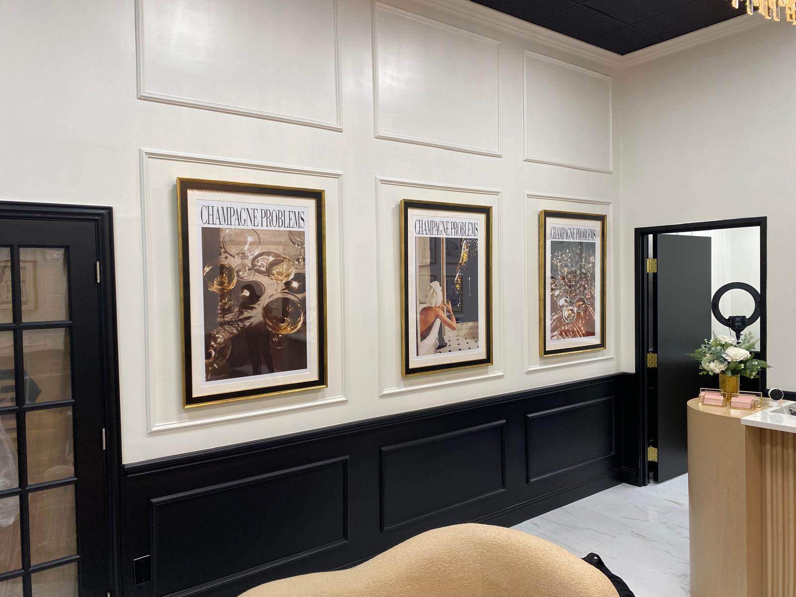 Three large gold-framed 'Champagne Problems' prints on a wainscoted salon wall