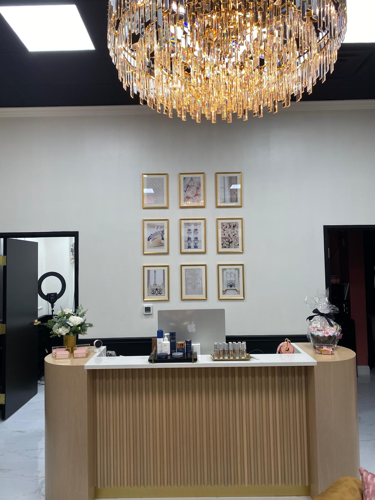 Grid of nine framed prints mounted beneath a crystal chandelier above a salon reception desk