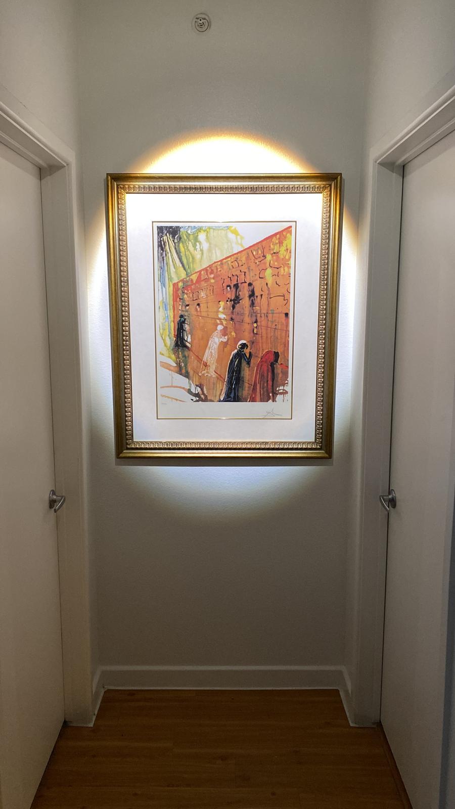 Large gold-framed lithograph backlit and centered at the end of a hallway